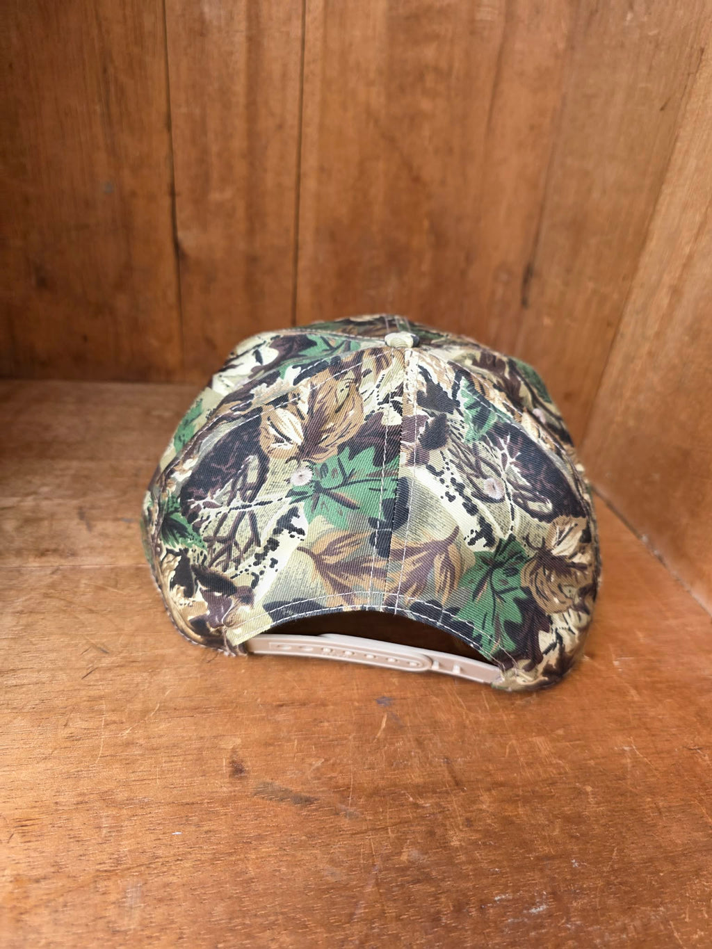 Country style camo baseball cap with statement western patch reading "Cowboys Make Better Lovers," photographed in soft golden hour lighting