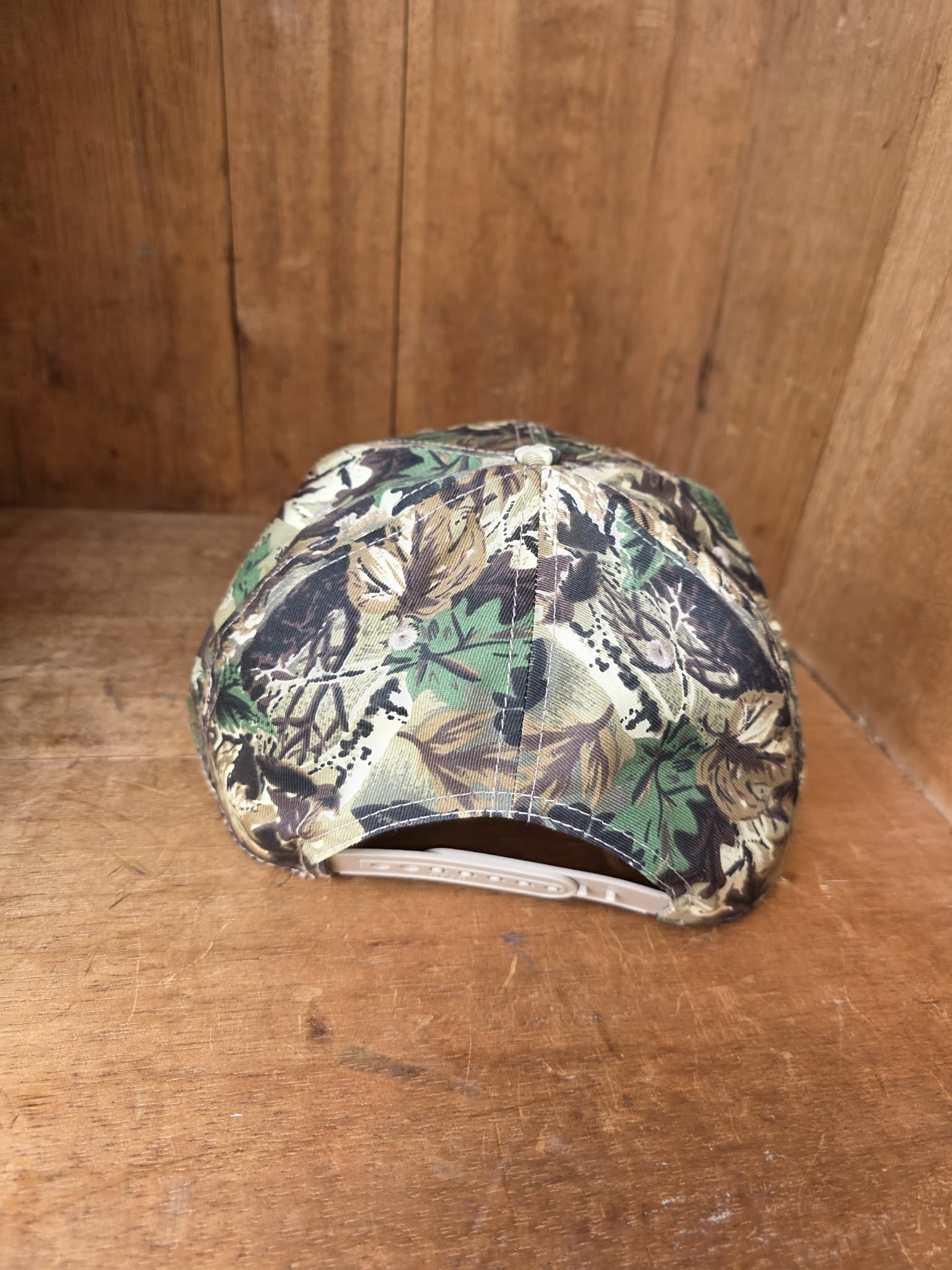 Country style camo baseball cap with statement western patch reading "Cowboys Make Better Lovers," photographed in soft golden hour lighting