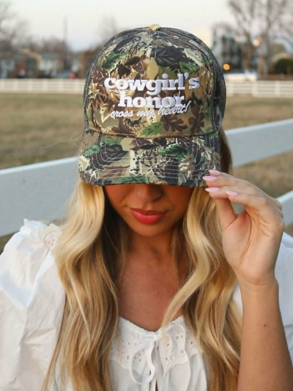 Camo trucker cap with white "cowgirls honor cross my heart" embroidery, mesh back panels, and a western inspired woodland print. Perfect country girl cap for rodeos, festivals, and everyday wear