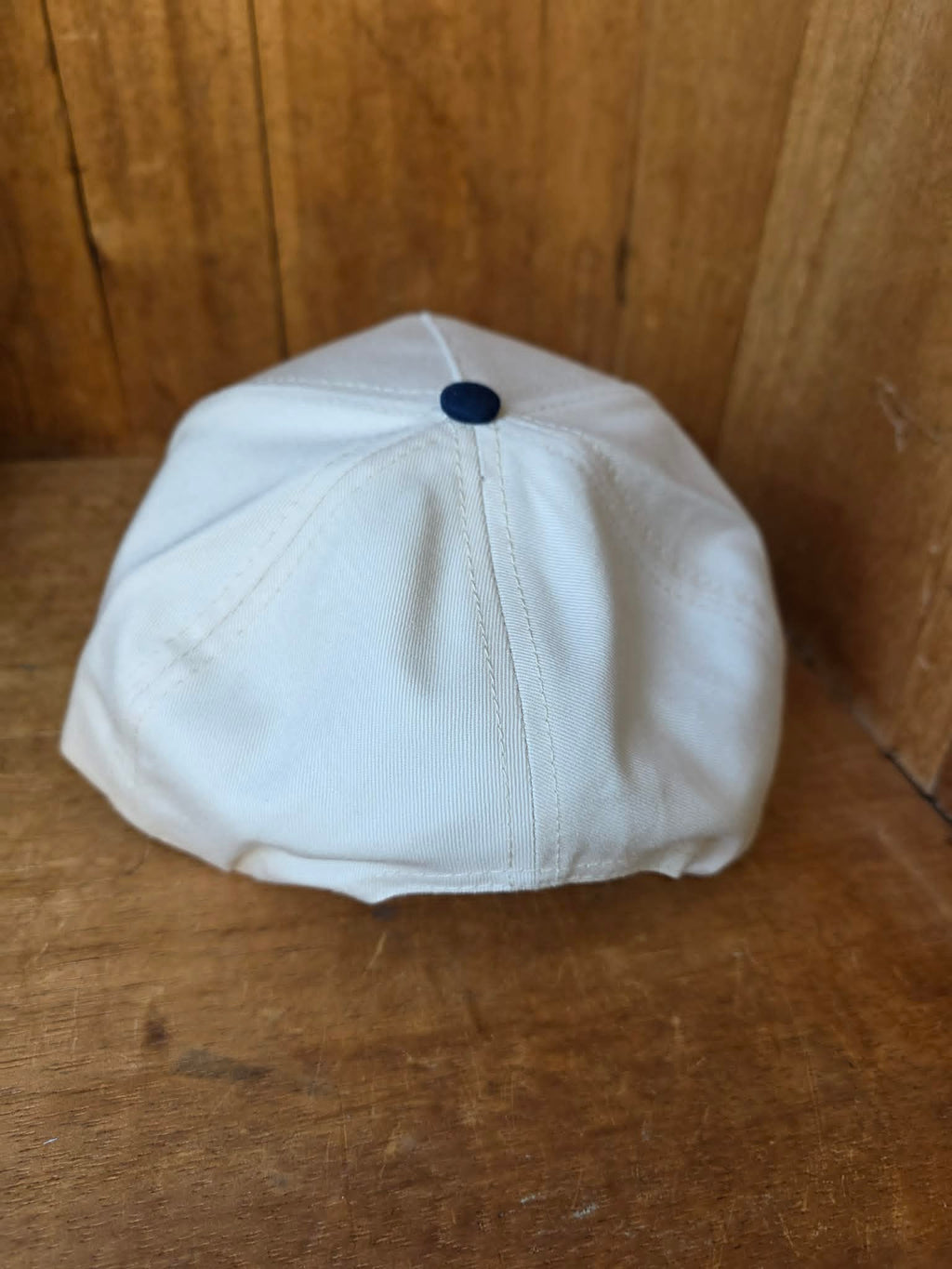 Cowgirl inspired trucker cap with navy brim and cream crown embroidered with "All Hat No Cattle Til The Cows Come Home" styled in a rustic outdoor setting