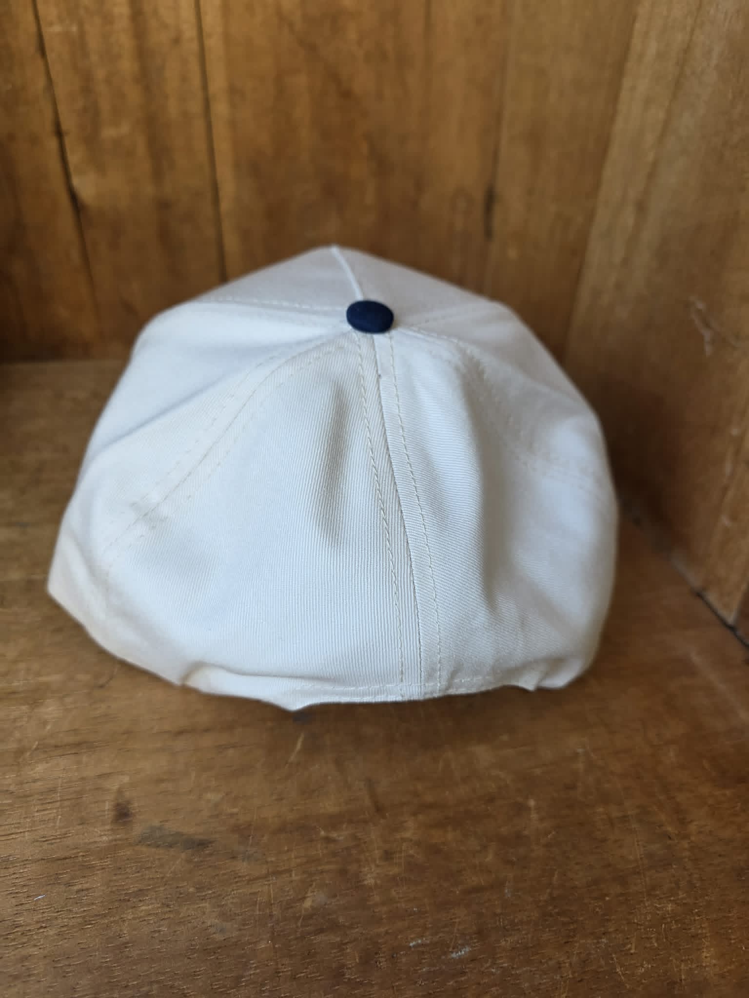 Cowgirl inspired trucker cap with navy brim and cream crown embroidered with "All Hat No Cattle Til The Cows Come Home" styled in a rustic outdoor setting