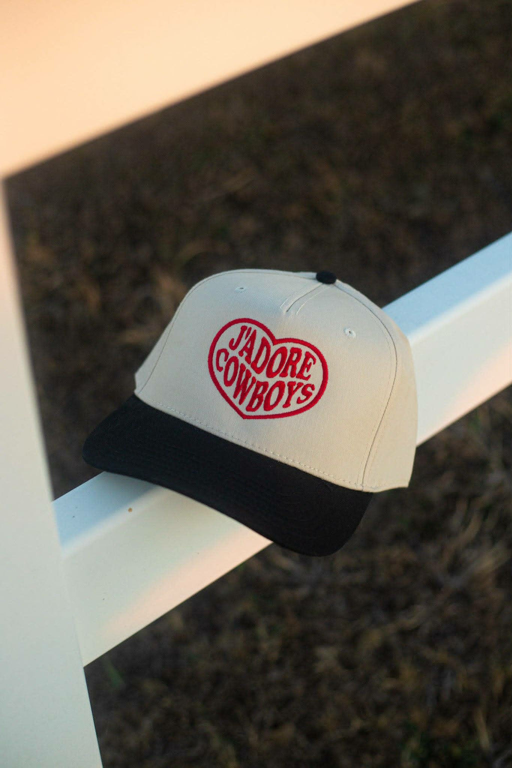 Cream and black trucker 
cap, featuring bold red embroidery in a heart shape reading "j"Adore Cowboys on front panel