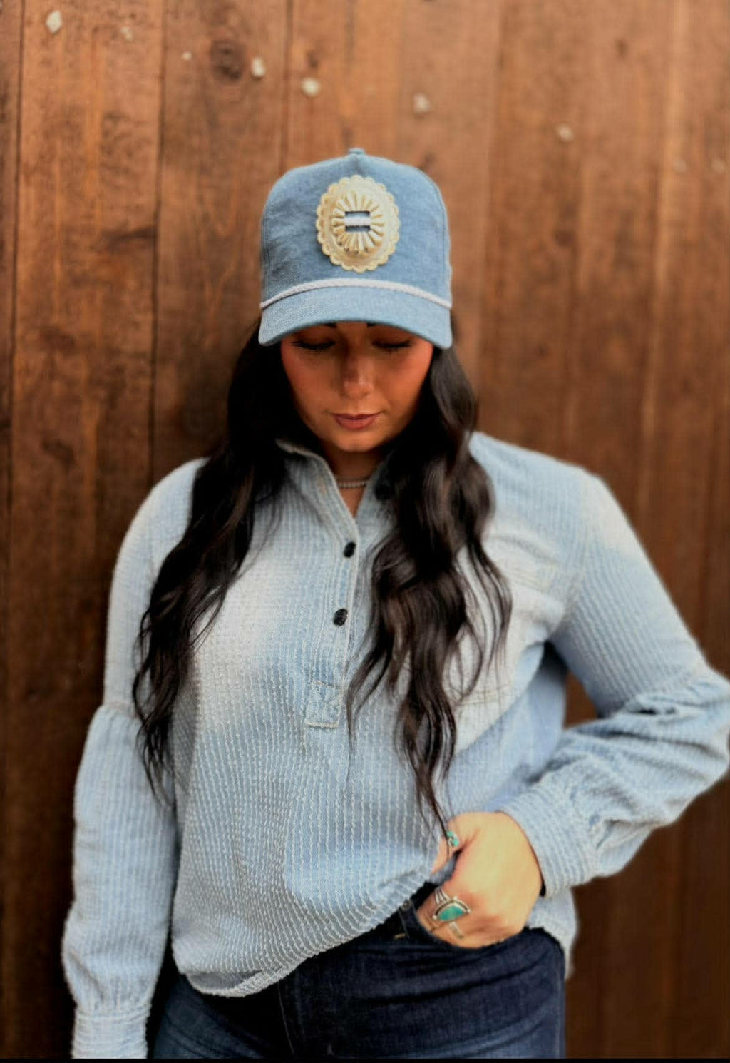 Denim trucker cap with a structured front panel featuring an embroidered poncho design on the front. The cap has a classic curved brim and a breathable mesh back, combining rugged Western style with a casual, everyday fit