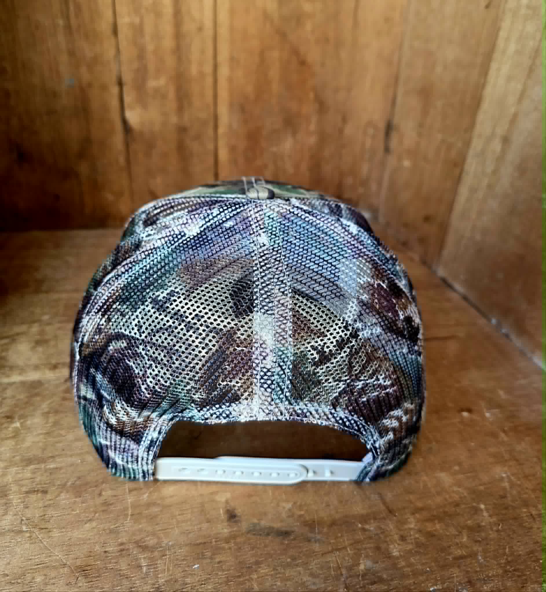 Rustic camo trucker hat with white statement embroidery, structured front panel, curved peak, and mesh backing. A bold western accessory for the cowgirls and country music lovers
