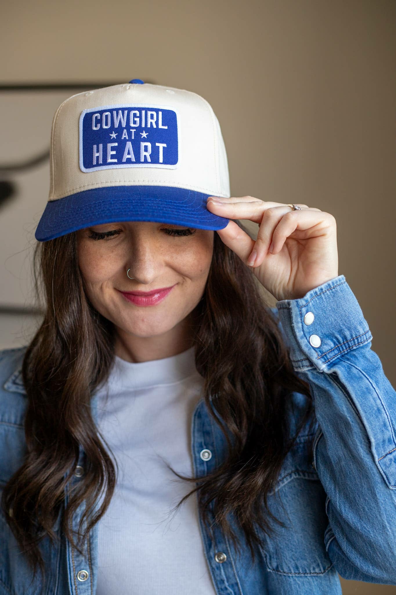 Two toned western trucker cap with white crown blue brim, showcasing a statement patch with "Cowgirl At Heart" in white lettering on a blue background