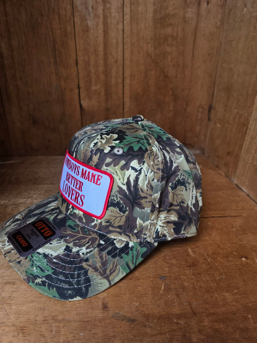 Dusty Cactus Co Camouflage trucker cap featuring embroidered "Cowboys Make Better Lovers" patch on a structured curved brim cap