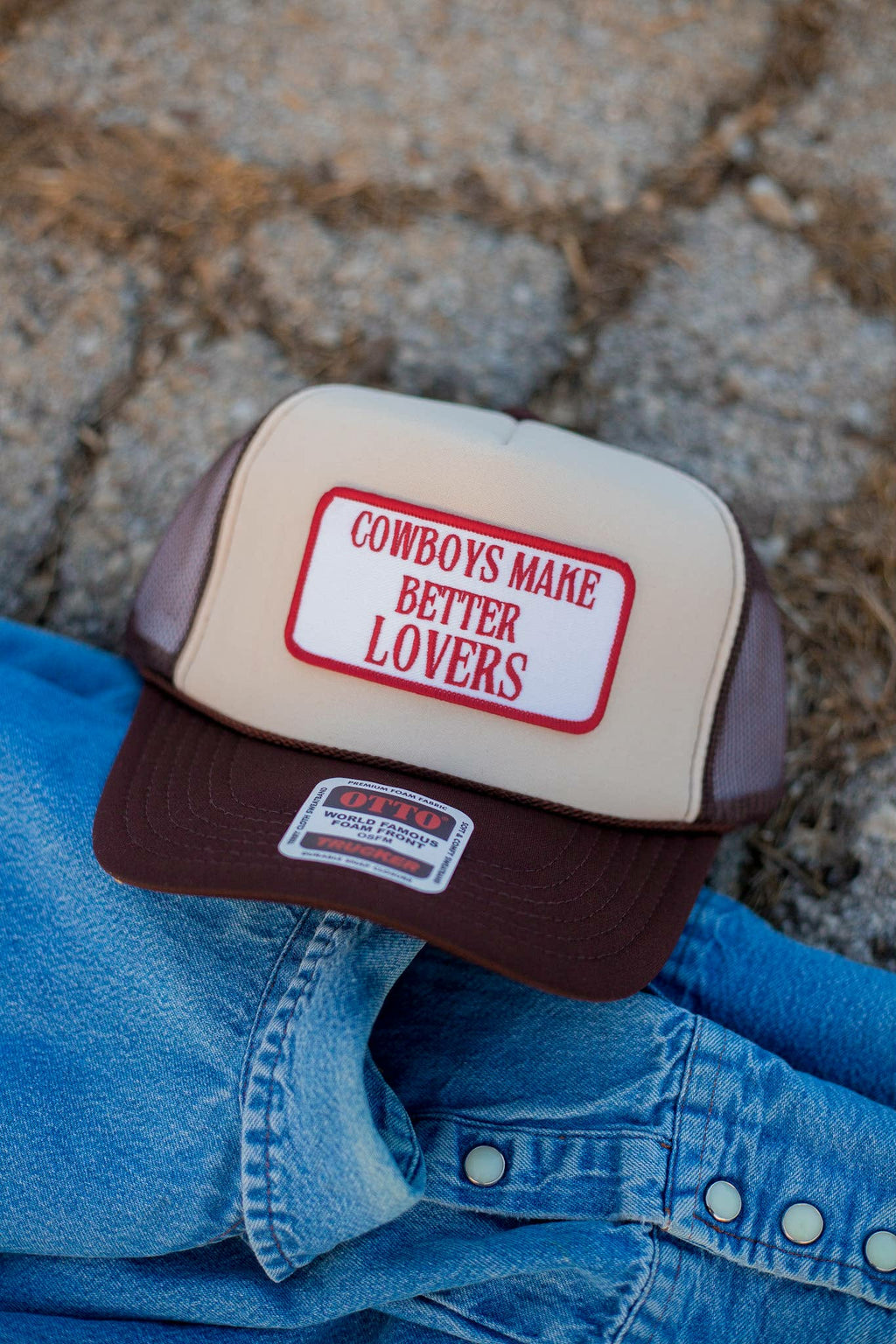beige and brown western trucker cap with structured front panel featuring Cowboys Make Better Lovers. The cap has a brown curved brim, mesh back