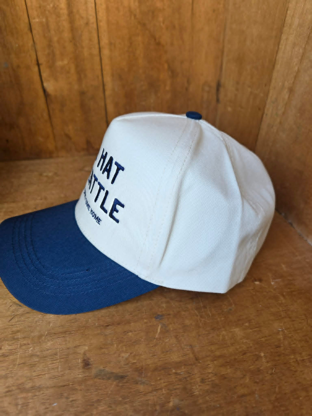 Close up lifestyle image of a cream and navy trucker cap featuring playful country style embroidery and curved brim styling