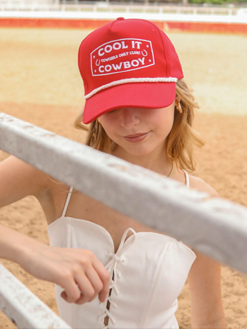 Western style red cap from Dusty Cactus Co with bold cowboy embroidery, horseshoe accents, and vintage inspired rope trim, styled flat lay with cowboy boots and lasso